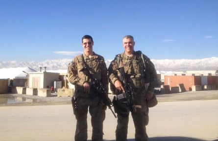 two men in military fatigues holding guns smile next to each other
