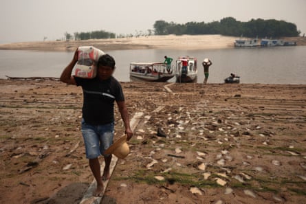 Sebastião Brito de Mendonça carries food donations, in the Santa Helena do Inglês community, in Iranduba. People in this area depend on the waterways for food supplies. In the distance, smoke from wildfires can be seen.