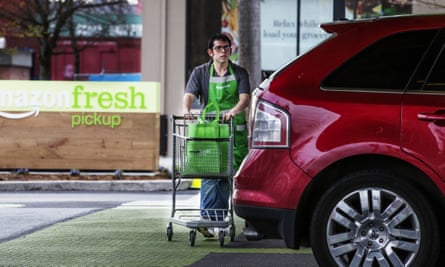 An AmazonFresh Pickup employee wheels grocery bags to a customer vehicle