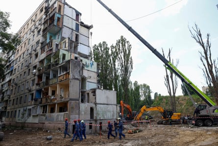 Rescuers walk past a partly destroyed apartment building