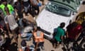 Palestinians crowd around a white car damaged in an airstrike