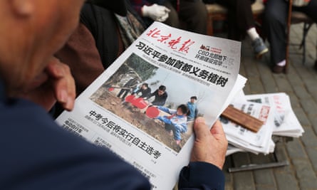 Man reads a newspaper featuring a photo of Chinese leaders attending a tree planting ceremony.