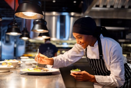 A female chef decorating a plate while serving food in a commercial kitchen.