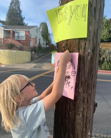 A child hangs up poster on telephone pole. The poster above reads “Be you” in childlike drawing.
