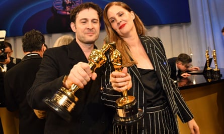 Arthur Harari and Justine Triet stand side by side clinking their Oscar statuettes together