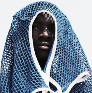 A young black man looks directly into the camera, his face only just visible through the arm-hole in a blue mesh vest that is draped over his head