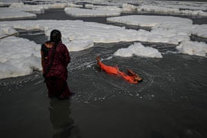 Women devotees take a dip in the waters of Yamuna river as a part of rituals for the upcoming Hindu festival of Chhat puja amid foam created by pollution in the water