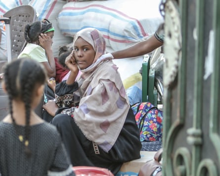 A Sudanese woman in a headscarf sitting down on a bench surrounded by baggage