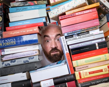Ioan Marc Jones peeking through a gap in a giant pile of classic books – only his face is visible