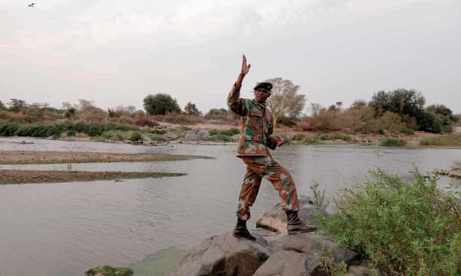 A man in army fatigues stands by a wide river.