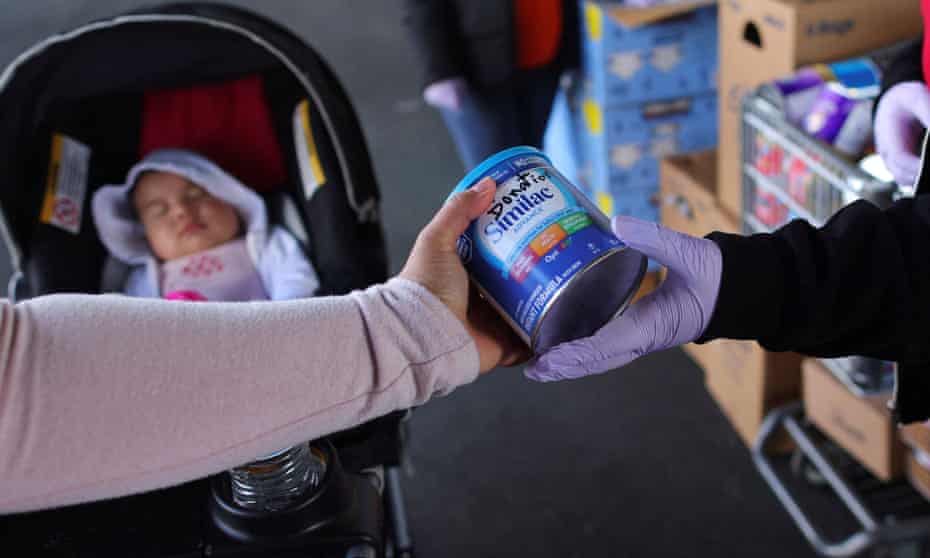 baby in stroller is visible behind mother's hand receiving formula from a clerk