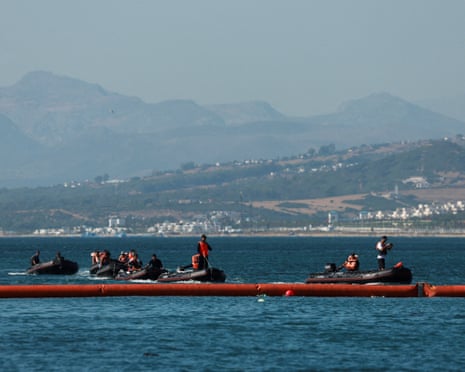 Members of the navy in boats behind floating orange tubes that mark the border