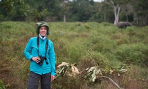 Kathleen Gobush stands in an open space. An elephant can be seen in the background.