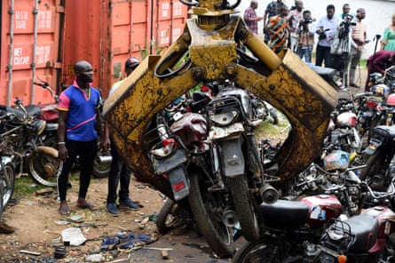 Two men stand to one side as crane lifts taxi motorcycles