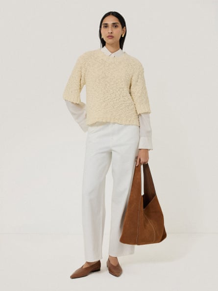 Model wearing cream jumper and shirt with cream jeans and a tan suede tote.