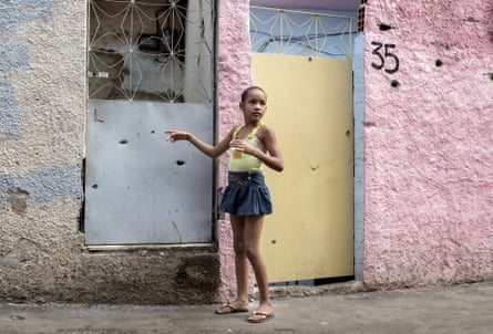 A young girl points to bullet holes in the front of her house in the Complexo do Alemão.
