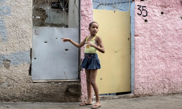 A young girl points to bullet holes in the front of her house in the favela Complexo do Alemao in Rio de Janeiro, Brazil. 