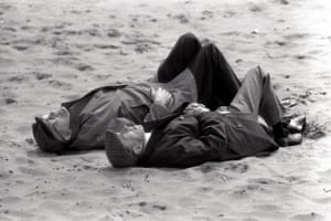 August Bank Holiday in Blackpool, 1971. Two elderly men in flat caps and coats asleep on the beach
