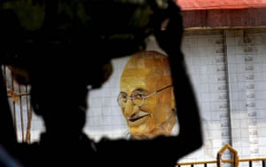 A vendor walks past next to a wall painting of Gandhi