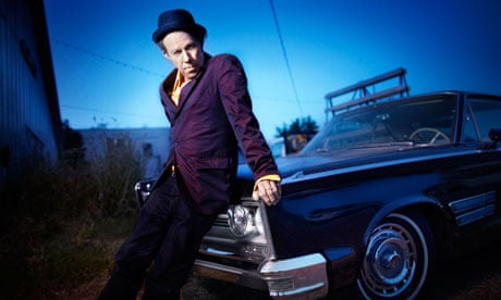 Tom Waits photographed sitting against the hood of a car