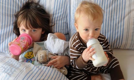 Little girls drinking from their bottles in bed