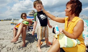 A mother applies sun cream to the face of a small child
