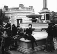 A young woman relaxes on the edge of the fountain in Trafalgar Square