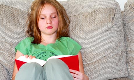 Young girl reading a book on a couch.