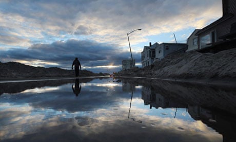Man walks by standing water and piles of sand swept onto a road from superstorm Sandy