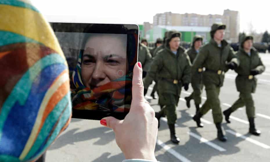 Russian servicemen march past a woman using a tablet during a military show 