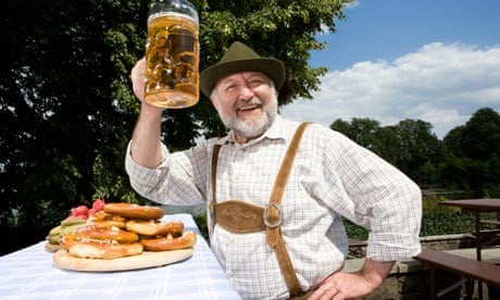 A traditionally clothed German man in a beer garden raising his beer glass in toast