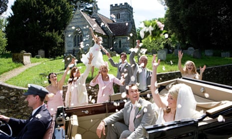 Wedding party throwing confetti on bride and groom in convertible vintage car by church, smiling