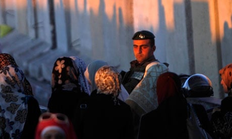 Palestinian women walk past an Israeli soldier