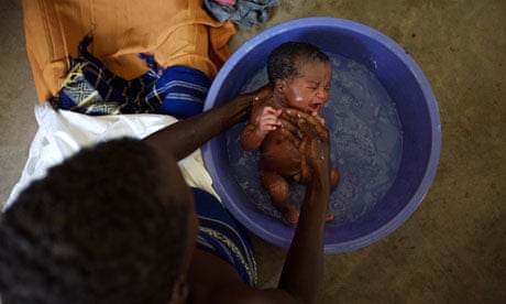 A baby is washed in a bowl at the Katine health centre