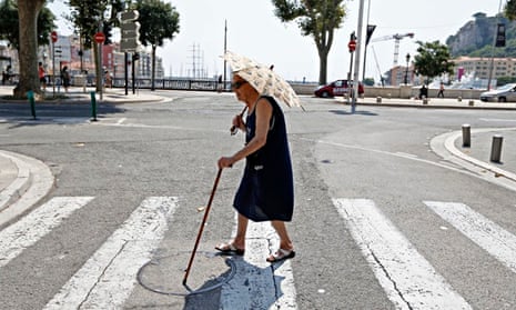 Elderly woman holding an umbrella crosses a street during summer heatwave in Nice, France