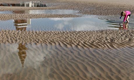 Blackpool Tower is reflected in a puddle as a girl plays on Blackpool beach