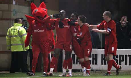 Jonathan Tehoue celebrates with Leyton Orient's mascot after scoring the equaliser against Arsenal