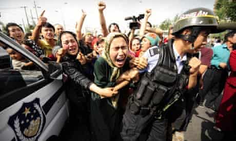 Ethnic Uighur women grab a riot policemen as they protest in Urumqi