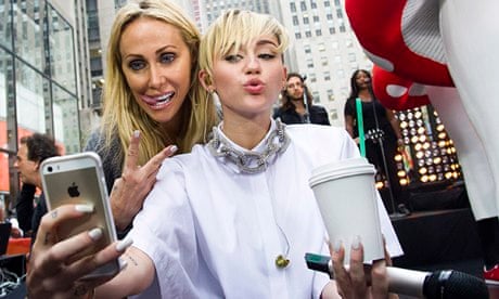 Miley Cyrus taking a photo of herself and her mother Tish (who has her tongue out)