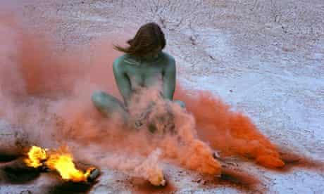 Judy Chicago’s photograph Immolation IV: woman sitting in desert surrounded by burning smoke flares