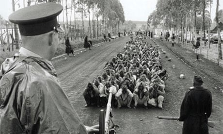 A colonial policeman and an auxiliary guard Mau Mau suspects in 1954