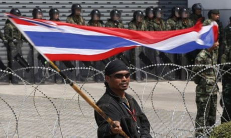 An anti-government protester waves a Thai flag as he stands in front of army soldiers.
