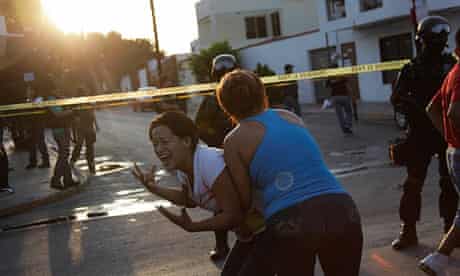 A woman is held back she reacts to the Gulf cartel's killing of three men and a woman in Monterrey