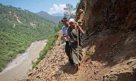 A pilgrim is helped by a villager along a path damaged by a landslide in the state of Uttarakhand