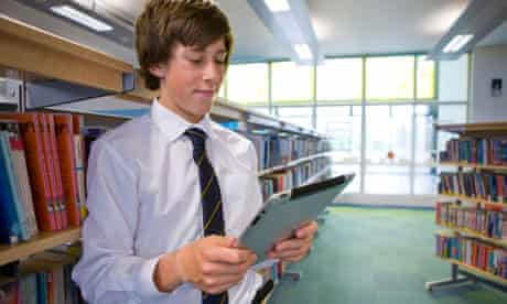 Male student reading electronic book on digital tablet in school library