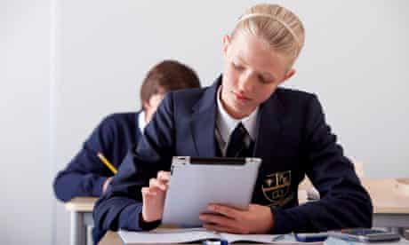 Female student in school uniform using digital tablet at desk in classroom