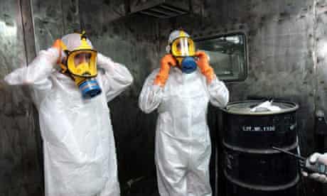 Two technicians in protective wear, alongside a box containig uranium ore concentrate, in Iran