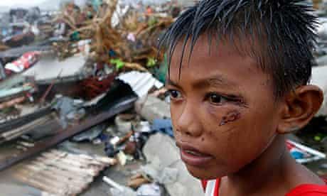 A boy who was wounded by flying debris in Typhoon Haiyan stands at the ruins of his family's house i