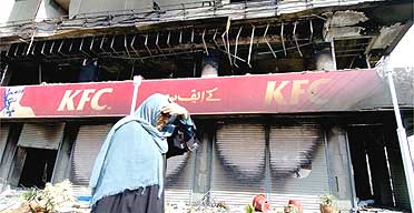 A woman walks past a burnt out KFC outlet in Karachi, Pakistan