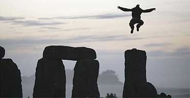 A man jumps in the air from the top of one of the stones as the sun rises over Stonehenge